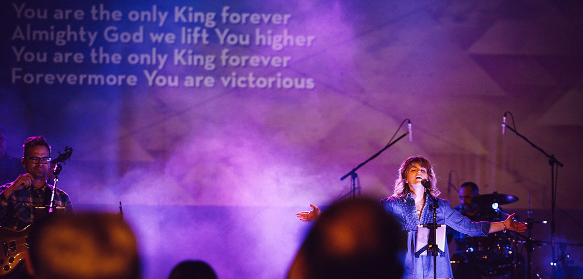 Female singer during time of worship with arms outstretched and words on screen