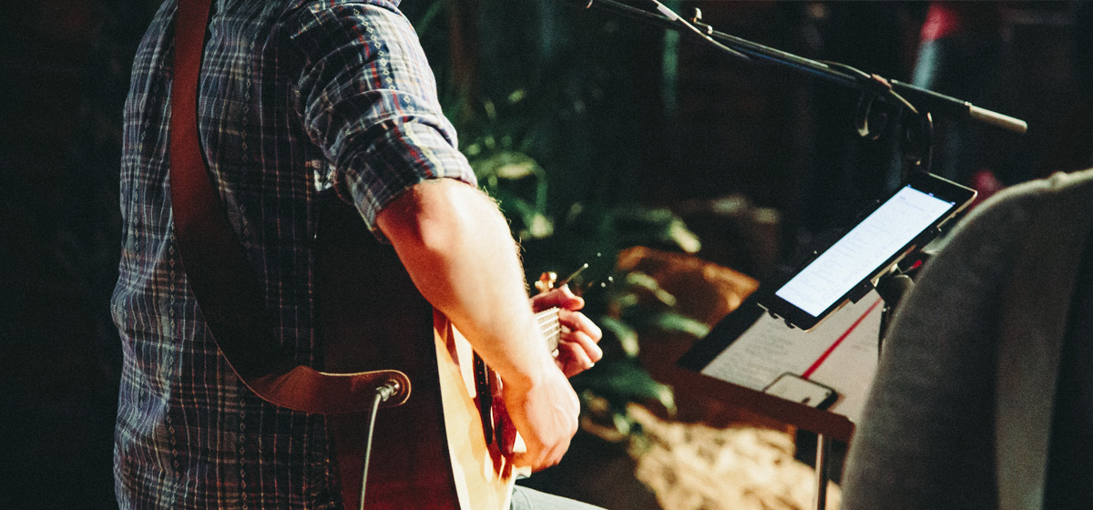 Man playing guitar and reading music from ipad