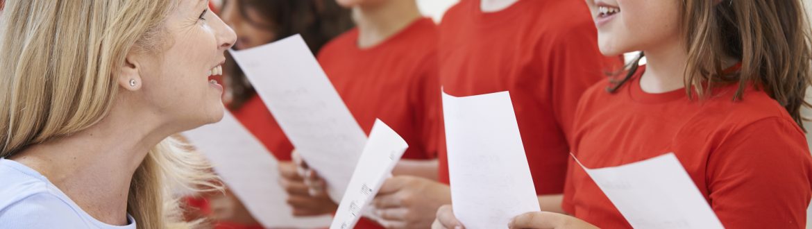 Children In Singing Group Being Encouraged By Teacher